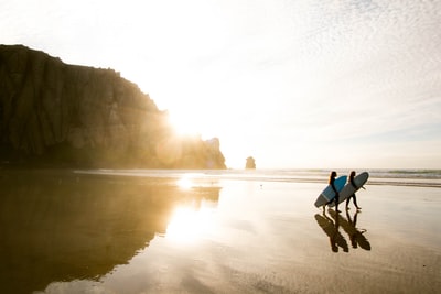 Two people to walk on the beach while holding a surfboard
